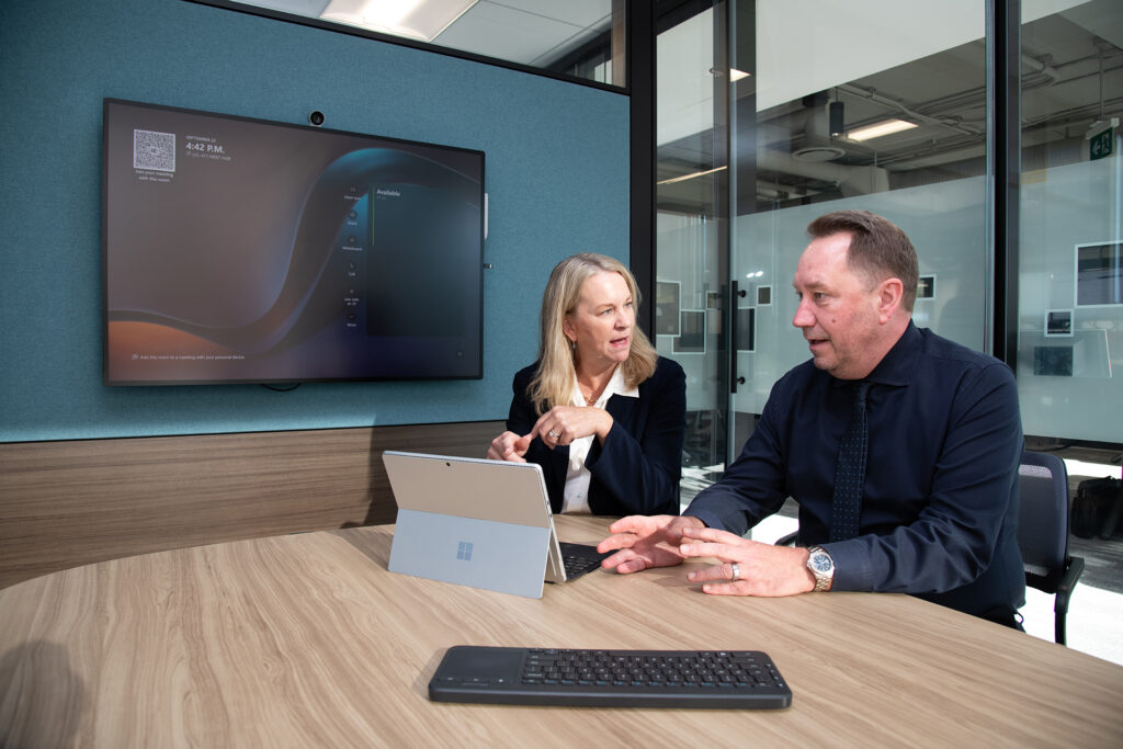 A man and a woman sit at a table in a conference room working on a Surface tablet