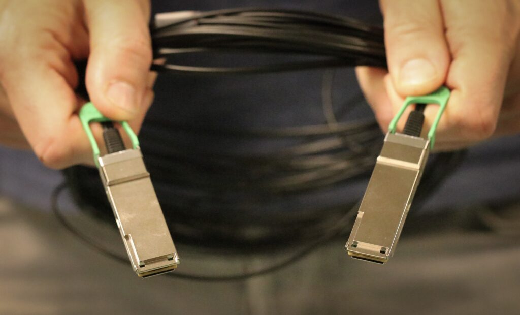 Les mains d’un homme tiennent une boucle de câble noir fin et deux boîtiers rectangulaires brillants, chacun de la taille d’un gros pouce humain.