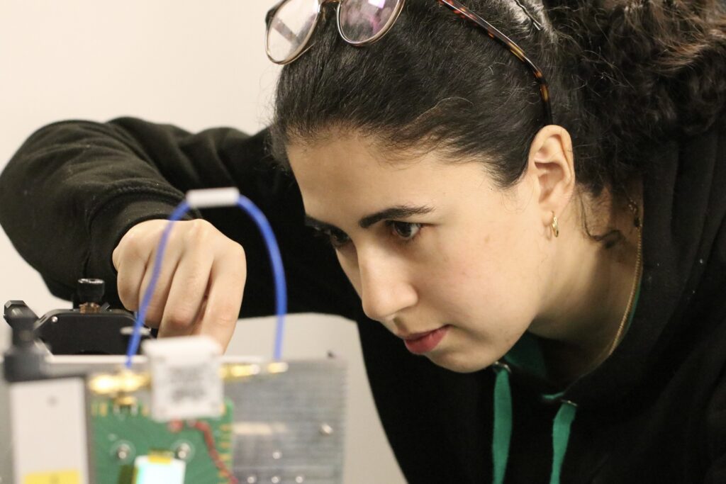 Gros plan d’une femme aux cheveux noirs frisés, concentrée sur un dispositif mécanique complexe.